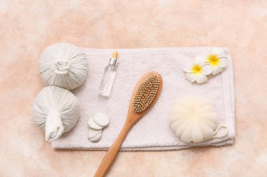 Spa taşları, masaj vücut fırçası, bitkisel torbalar, banyo süngeri, bir şişe serum ve pembemsi çiçekler pembe grunge arka planda.