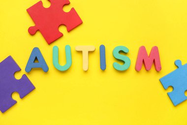Kelime AUTISM ve sarı arka planda renkli yapboz parçaları. Üst görünüm