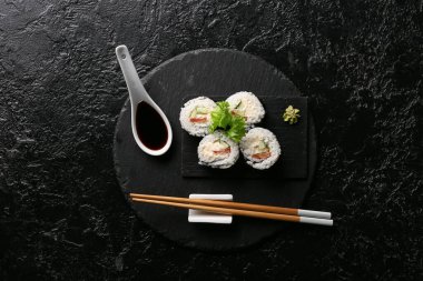 Lezzetli suşi ruloları ve çubuklar, siyah grunge arkaplanda soya soslu kaşık.