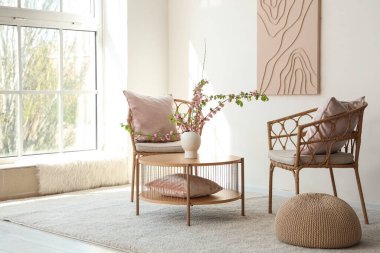 Oturma odasında vazo ve çiçek açan dalları olan sandalyeler ve kahve masası.