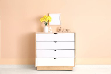 Oturma odasındaki çekmecelerin üzerinde nergis çiçekleri olan vazo.