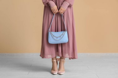 Yüksek topuklu ayakkabılar ve bej duvarın yanında çanta taşıyan pembe elbiseli şık genç bir kadın.