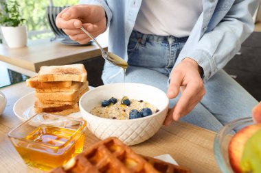 Genç kadın mutfaktaki lezzetli yulaf ezmesine tatlı bal ekliyor.