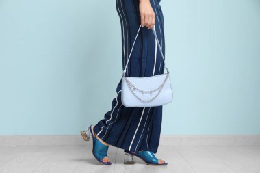 Pantolon ve topuklu ayakkabılı şık genç kadın mavi duvarın yanında el çantalı.