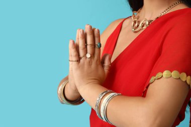 Beautiful young Indian woman in traditional sari praying on blue background, closeup. Divaly celebration