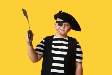 Sarı arka planda cadılar bayramı partisi için korsan gibi giyinmiş sevimli, mutlu çocuk.