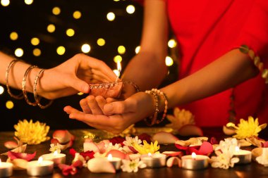 Diwali için güzel bir diya lambası tutan kadınlar. Karanlık arka planda mumlar, çiçekler ve yapraklarla.