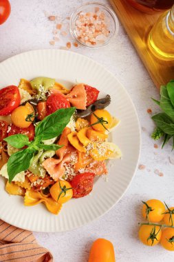 Beyaz arka planda domates ve fesleğenli bir tabak lezzetli farfalle makarna.