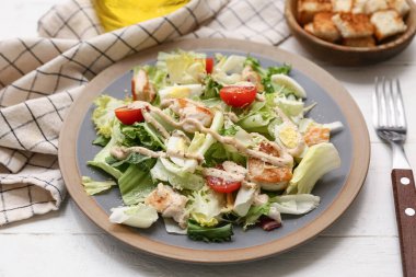 Plate with tasty chicken Caesar salad and bowl of croutons on white wooden background, closeup