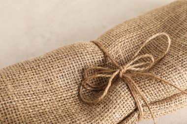 Burlap fabric tied with rope on light background, closeup