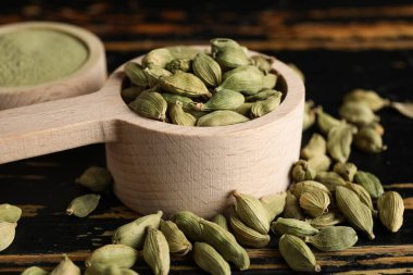 Spoons with cardamom spice and powder on black wooden background, closeup