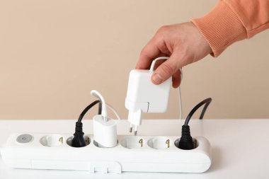 Erkek el uzatma kablosundan şarj aletini çıkartıyor. Bej duvarın yanındaki masada, yakın plan.