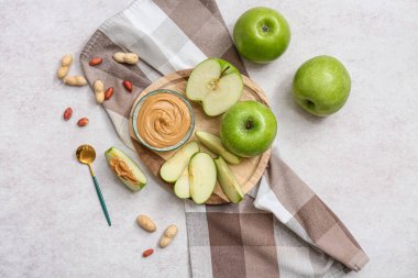 Wooden plate with fresh apples and bowl of sweet peanut butter on white background