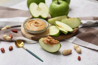 Wooden plate with fresh apples and bowl of sweet peanut butter on white background, closeup