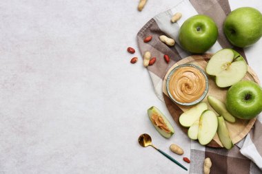 Wooden plate with fresh apples and bowl of sweet peanut butter on white background