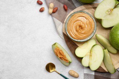 Wooden plate with fresh apples and bowl of sweet peanut butter on white background