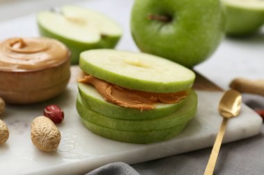 Cutting board with fresh apple sandwich with sweet peanut butter on white background, closeup