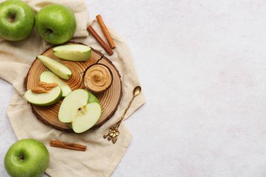 Wooden board with cut fresh apple, cinnamon and bowl of sweet peanut butter on white background