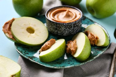 Plate of fresh apple slices with sweet peanut butter on blue background, closeup