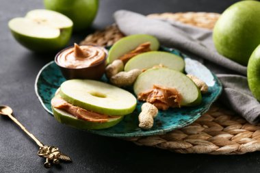 Plate of fresh apple slices with sweet peanut butter on black background, closeup