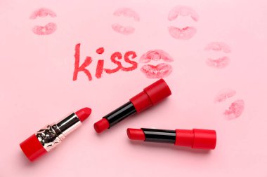 Word KISS written with red lipsticks on pink background