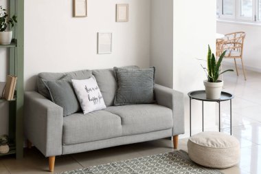 Modern interior of living room with comfortable grey sofa and soft pouf