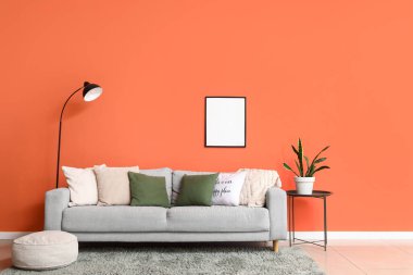 Comfortable grey sofa with soft pillows and floor lamp near orange wall in living room