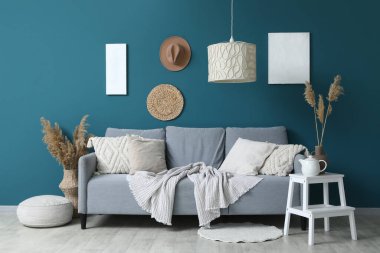 Oturma odasındaki mavi duvarın yanında yumuşak yastıklı, rahat gri kanepe.