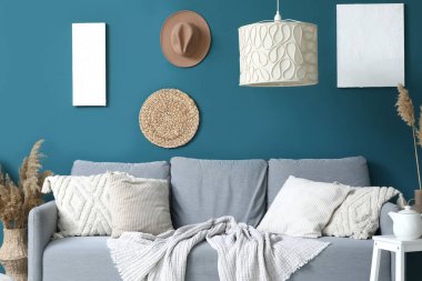 Yumuşak yastıklı rahat gri kanepe ve mavi duvarın yanında asılı lamba, oturma odasında, yakın çekim