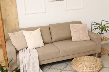 Comfortable brown sofa and wicker pouf near white wall in living room