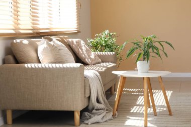 Oturma odasının penceresinin yanında masaları ve çiçekleri olan rahat kahverengi bir kanepe.