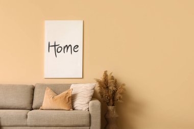 Yumuşak yastıklı rahat kahverengi kanepe ve oturma odasındaki bej duvarın yanında otlar, yakın plan.