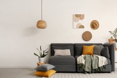 Yumuşak yastıklı rahat siyah kanepe ve oturma odasındaki beyaz duvarın yanında bitkiler.