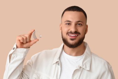Bej arka planda işitme cihazı olan genç adam, yakın plan.