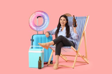 Young businesswoman in deck chair with beer and suitcase on pink background. Summer vacation concept