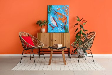 Şık oturma odasının içinde koltuklar, kahve masası ve turuncu duvarın yanındaki ahşap dolap.