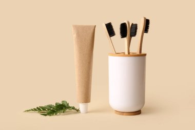 Bej arka planda bambu diş fırçası, yaprak ve tüp macunu olan tutucu