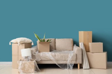 Taşındığı gün mavi duvarın yanında film ve kutularla dolu gri kanepe.