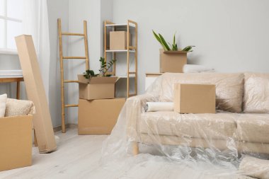 Sofa with film and boxes in living room on moving day