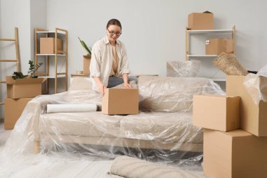 Young woman with moving box on sofa in room