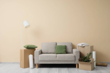 Taşındığı gün bej duvarın yanında kutuları olan gri kanepe.