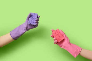 Hands in rubber gloves holding sponges for cleaning on green background