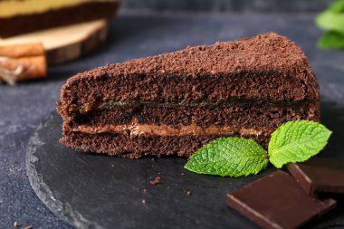 Koyu arkaplanda çikolata parçalı siyah tahta ve nane yaprakları, yakın plan.