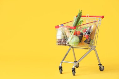 Sarı arka planda farklı taze ürünleri olan alışveriş arabası.