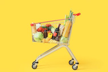 Sarı arka planda farklı taze ürünleri olan alışveriş arabası.