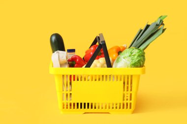 Sarı zemin üzerinde farklı taze ürünler olan alışveriş sepeti.