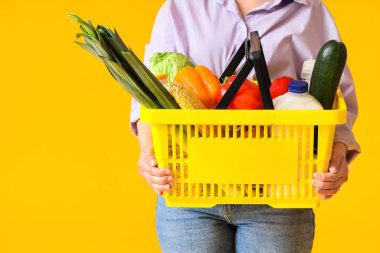 Woman holding shopping basket with different fresh products on yellow background