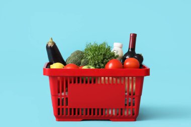 Kırmızı alışveriş sepeti ve mavi arka planda farklı taze ürünler.