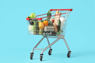 Mavi arka planda farklı taze ürünleri olan alışveriş arabası.