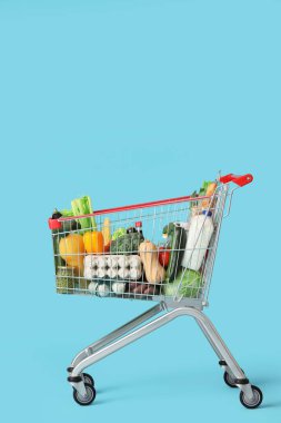 Mavi arka planda farklı taze ürünleri olan alışveriş arabası.